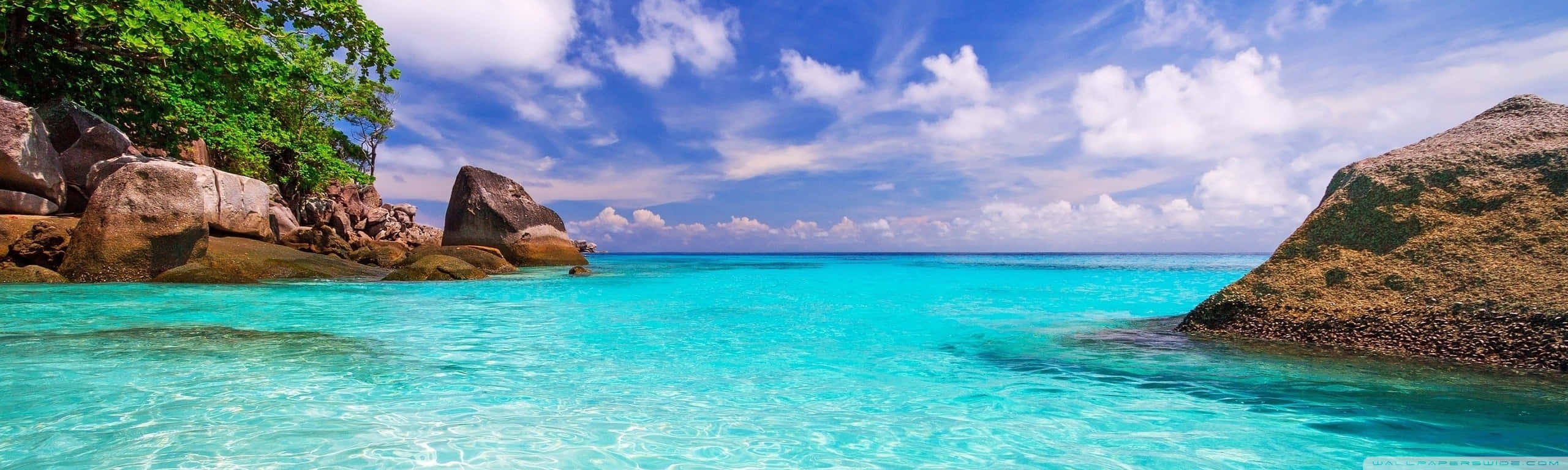 A Beautiful Blue Ocean With Rocks And Trees Wallpaper