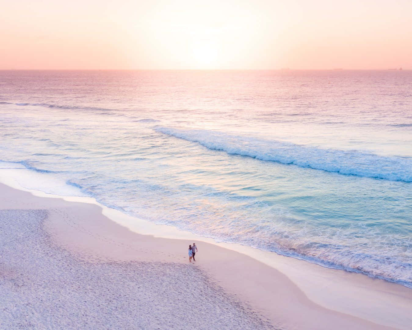 A Couple Walking On The Beach At Sunset Wallpaper