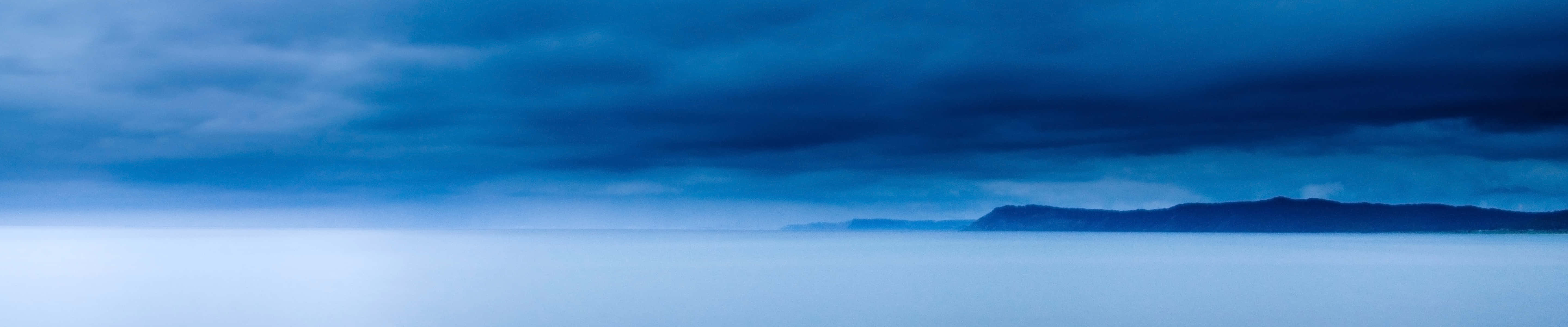 A Dark Sky Over The Ocean With Mountains In The Background Wallpaper