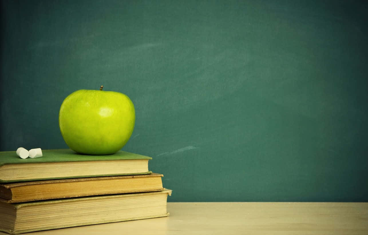 A Green Apple Sits On Top Of A Stack Of Books Wallpaper