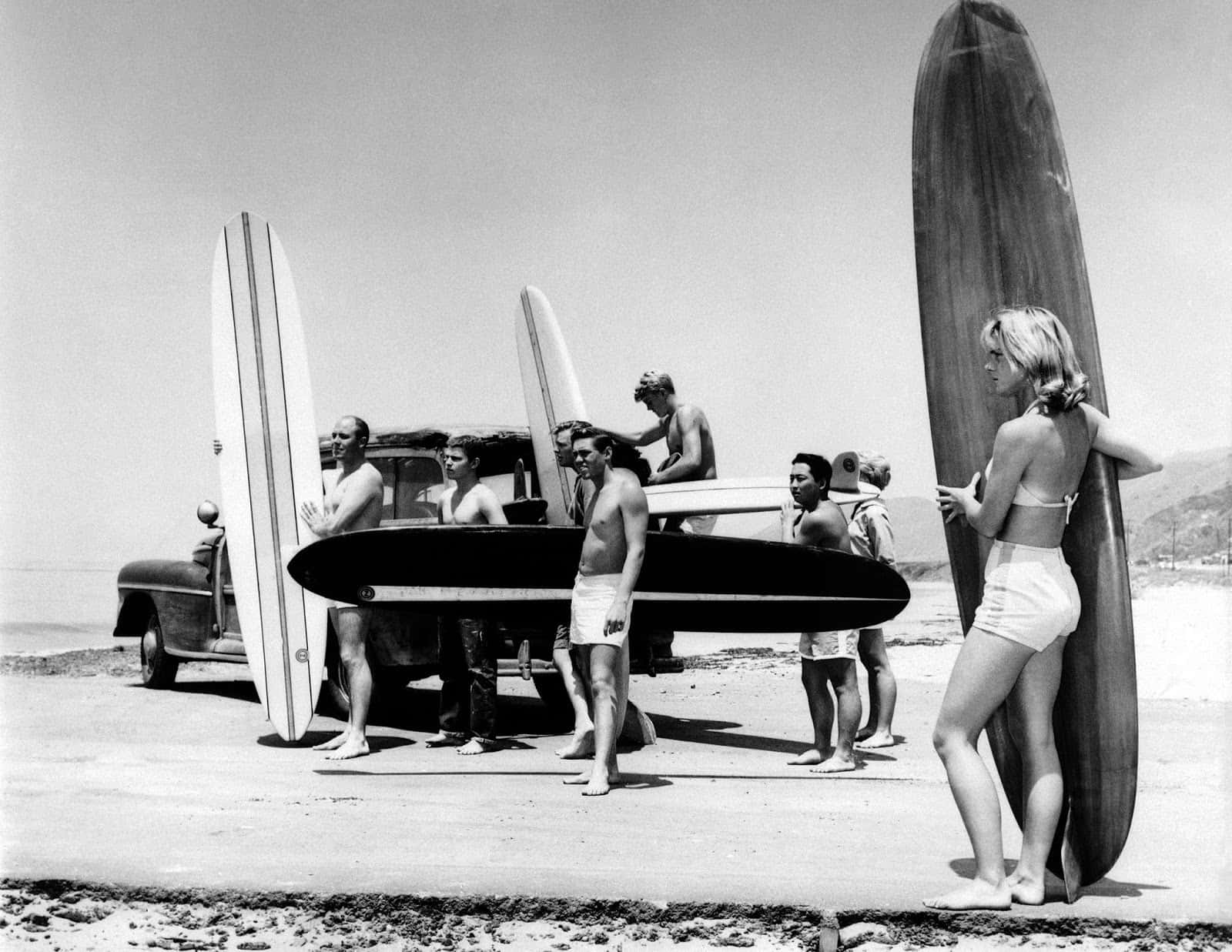 A Group Of People Standing Near A Truck With Surfboards Wallpaper