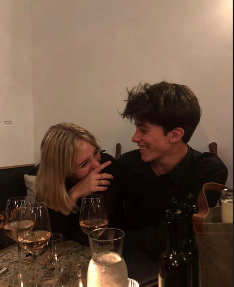 A Man And Woman Are Sitting At A Table With Wine Glasses Wallpaper