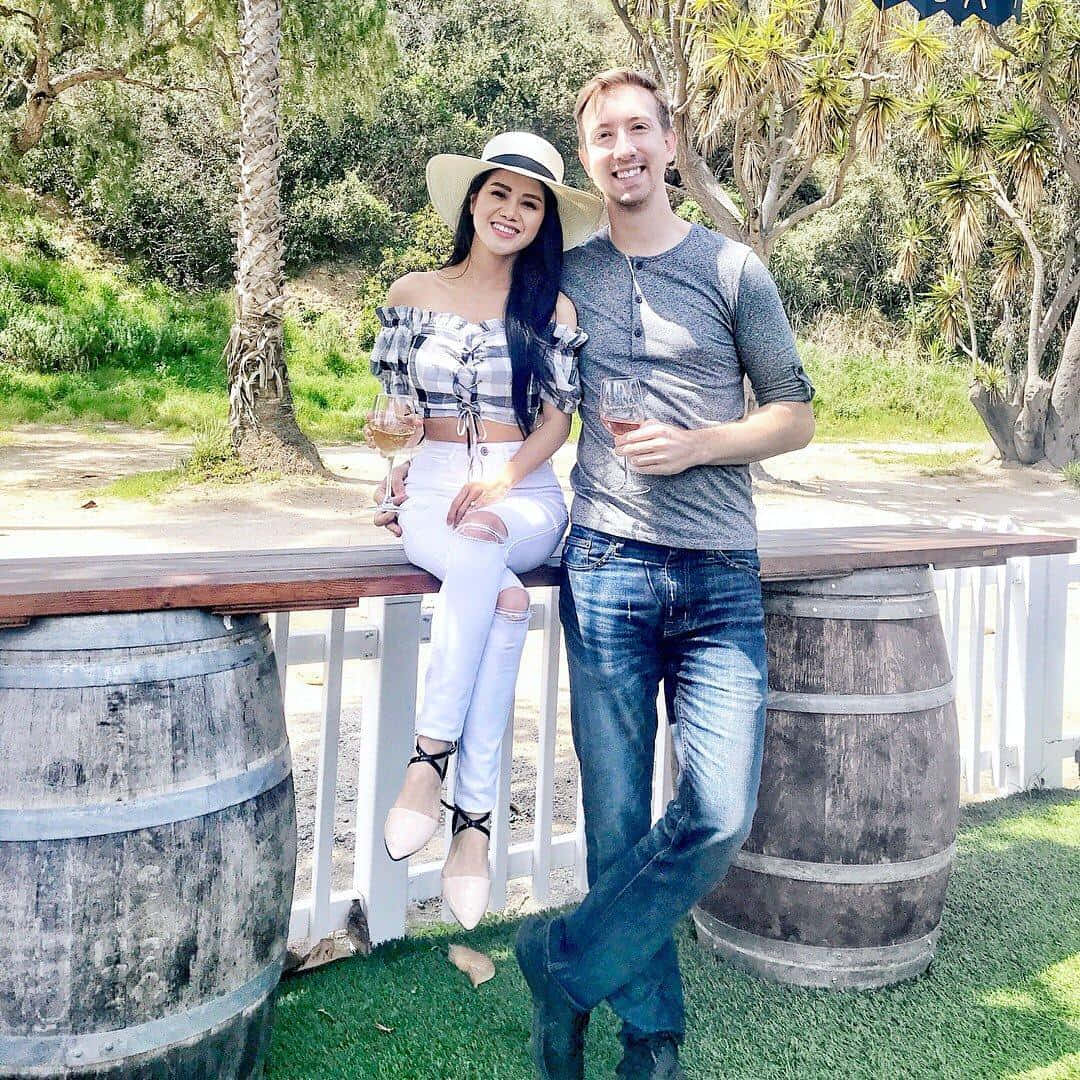 A Man And Woman Standing Next To A Wooden Barrel Wallpaper