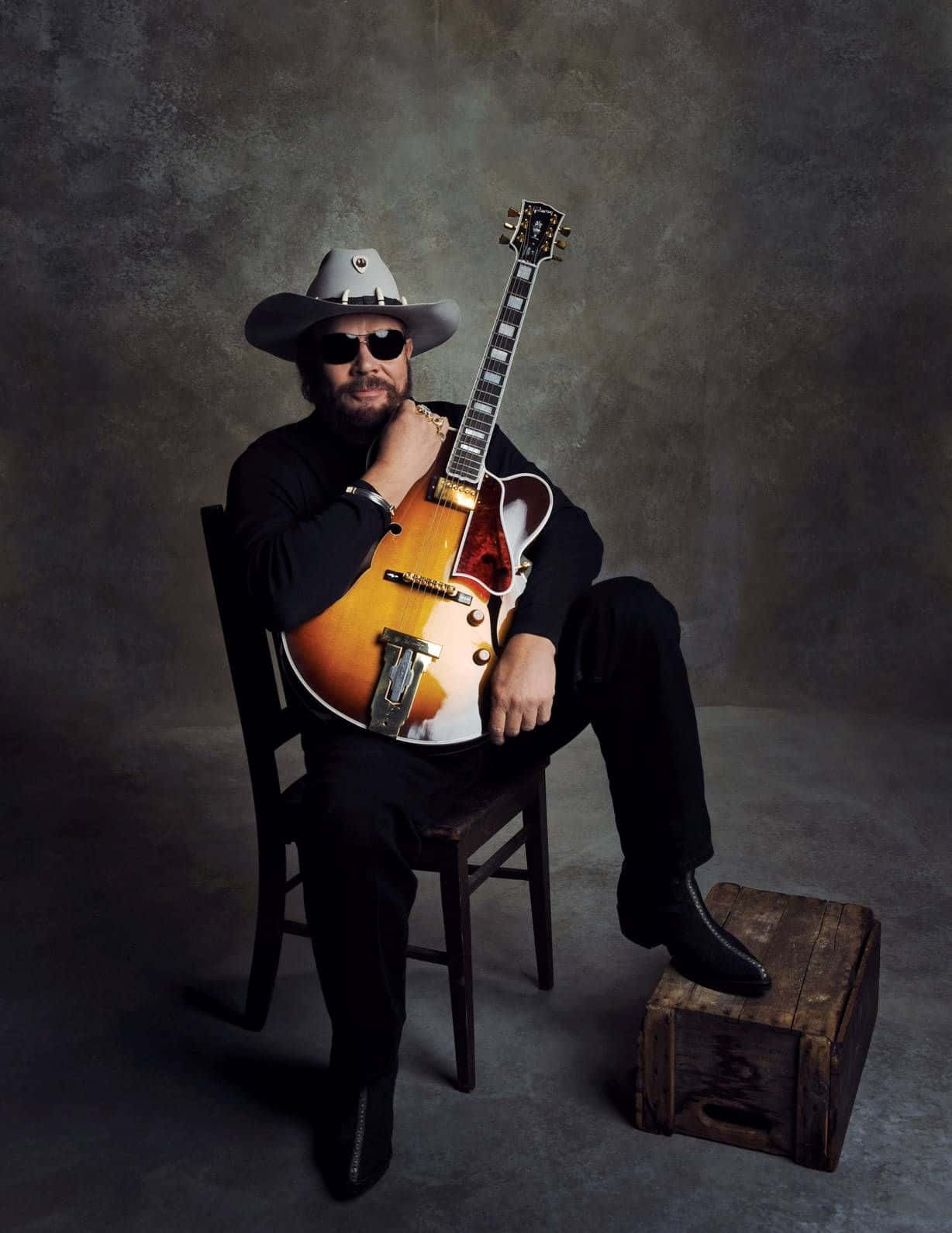 A Man In A Hat And Cowboy Hat Sitting On A Chair With A Guitar Wallpaper