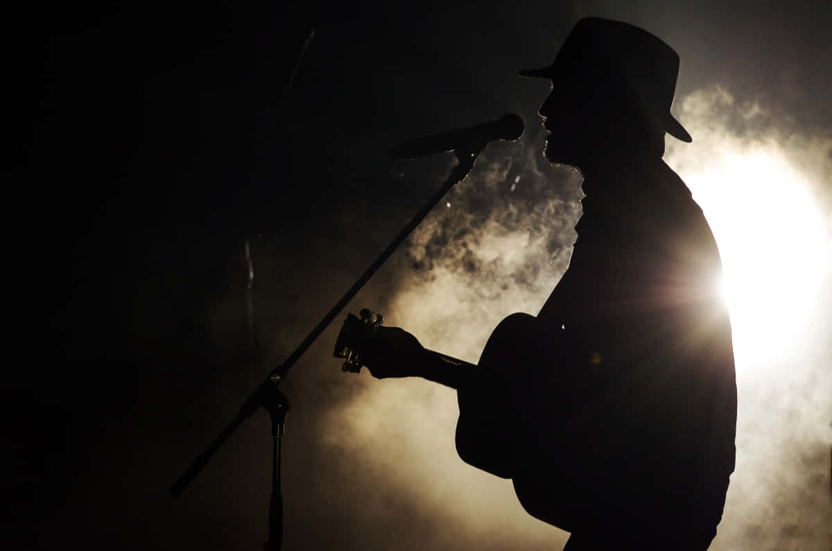 A Man In A Hat Is Playing An Acoustic Guitar Wallpaper