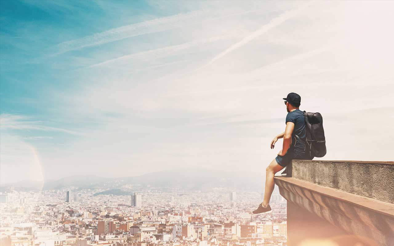 A Man Is Sitting On A Ledge Overlooking A City Wallpaper