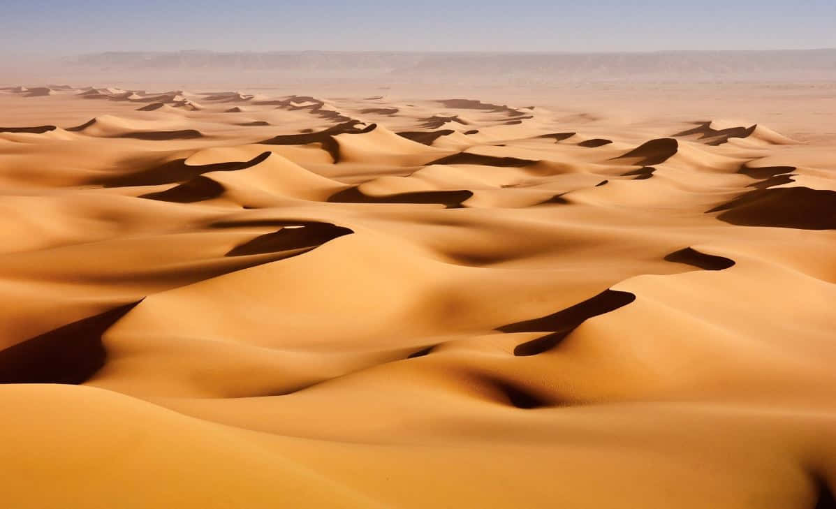 A Mesmerizing View Of Sand Dunes Under The Vast Blue Sky. Wallpaper