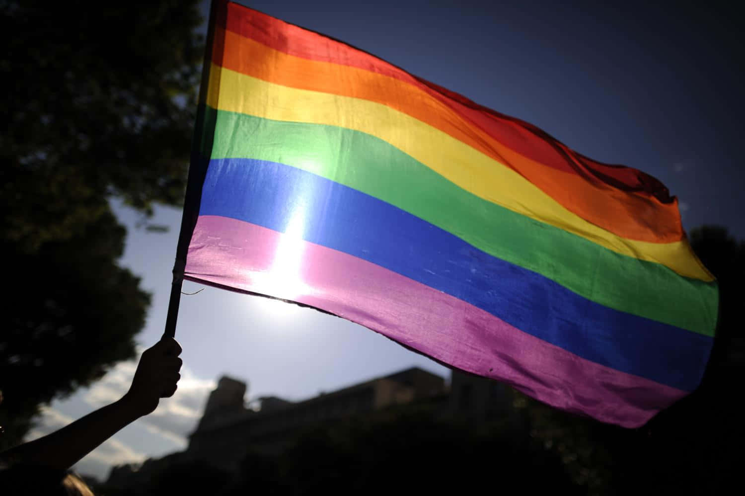 A Person Is Holding A Rainbow Flag In Front Of A Building Wallpaper