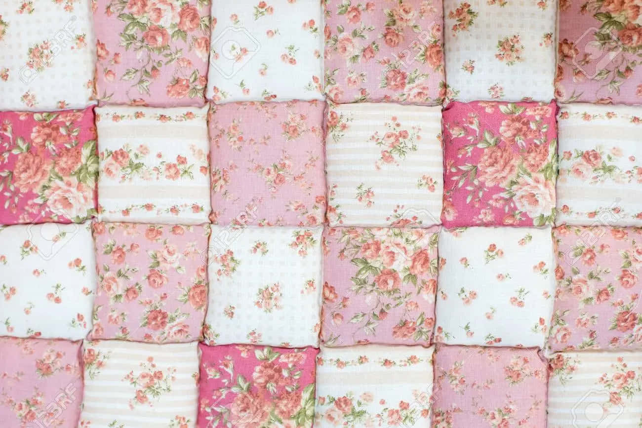 A Pink And White Quilt With Floral Patterns Wallpaper