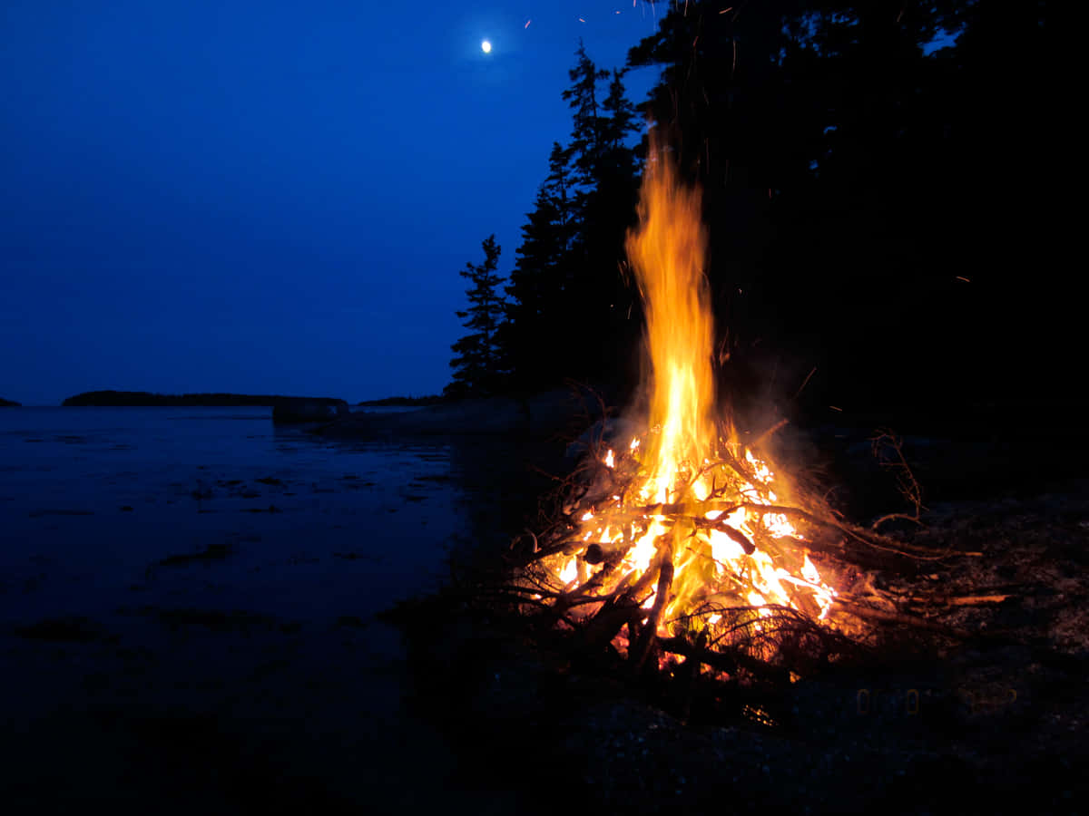 A Serene Beach Bonfire Under The Starry Sky Wallpaper