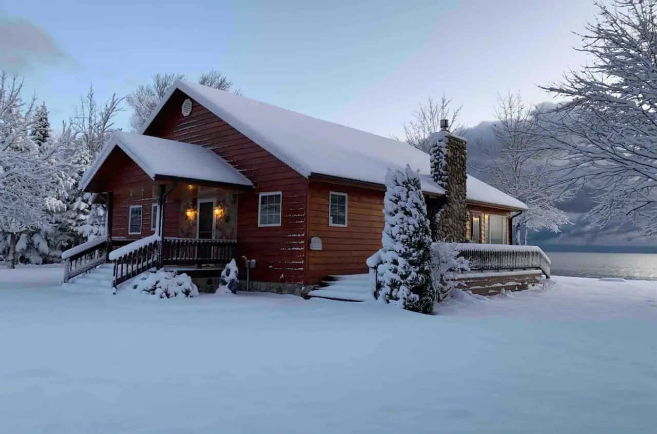 A Snow-covered Cozy Winter Cabin Nestled Among Tall Trees Wallpaper