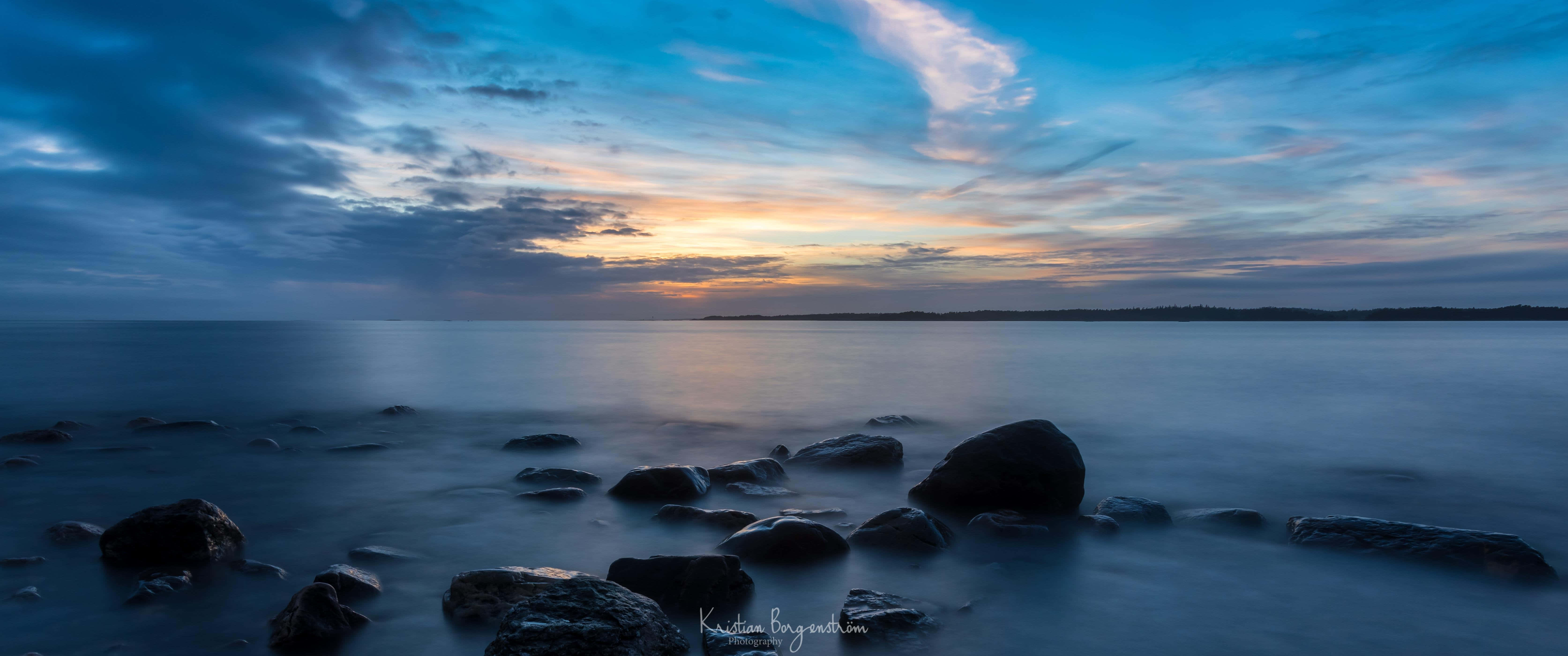 A Sunset With Rocks And Water In The Background Wallpaper