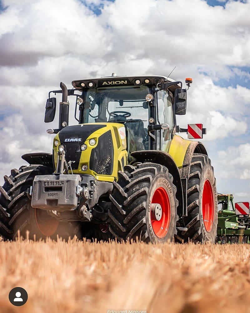 A Tractor Driving Through A Field With A Cloudy Sky Wallpaper