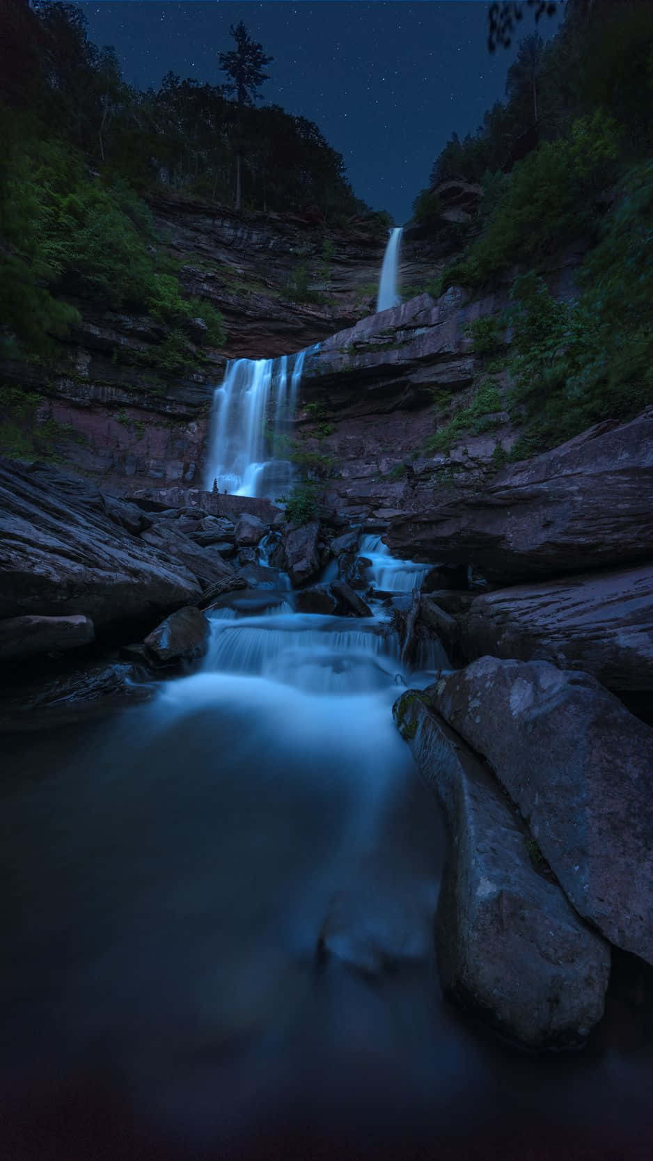 A Waterfall In The Dark With Stars Above It Wallpaper