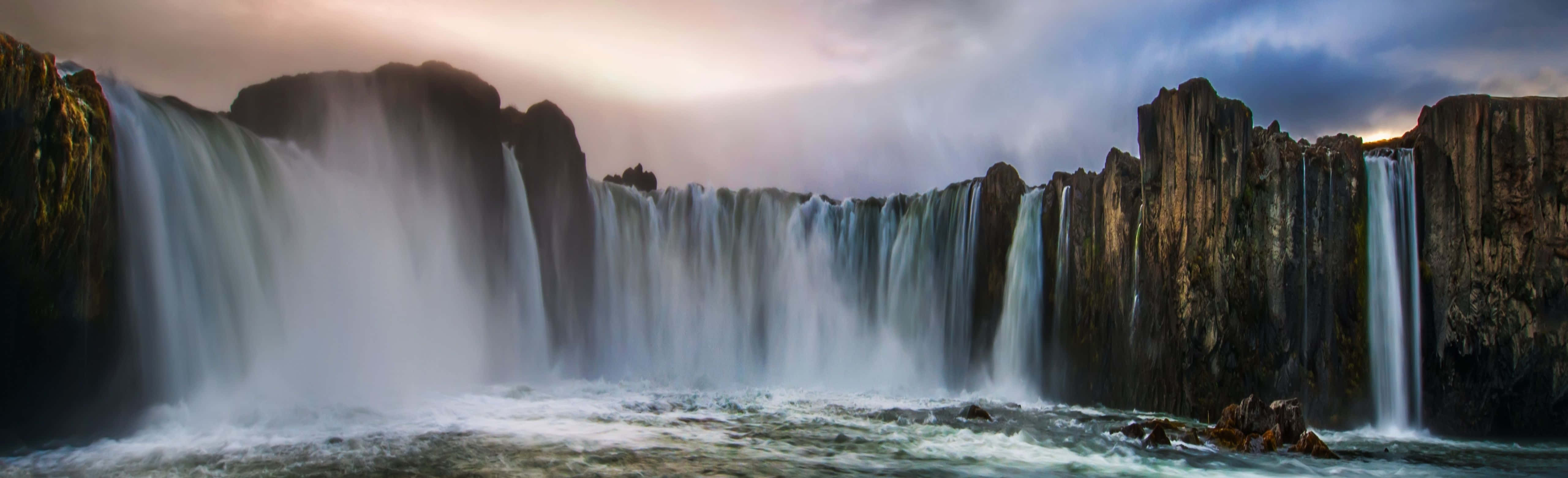 A Waterfall With A Cloudy Sky And Rocks Wallpaper