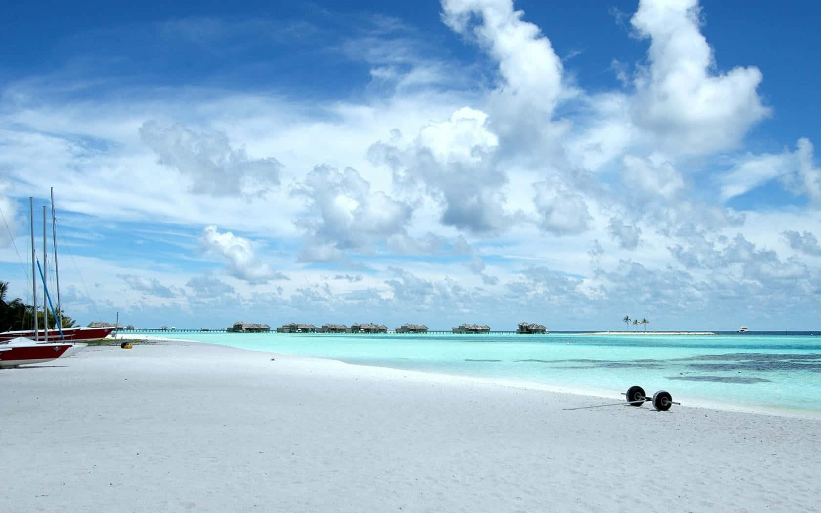 A White Sandy Beach With Boats And Sails Wallpaper