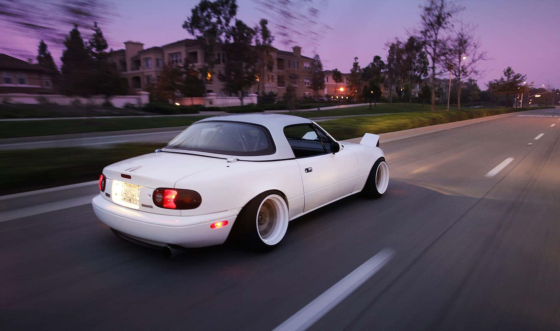 A White Sports Car Driving Down The Street At Dusk Wallpaper