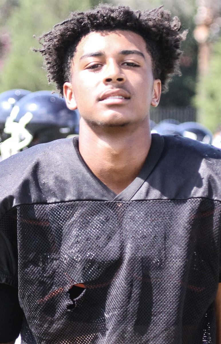 A Young Man In A Football Uniform Standing On The Field Wallpaper