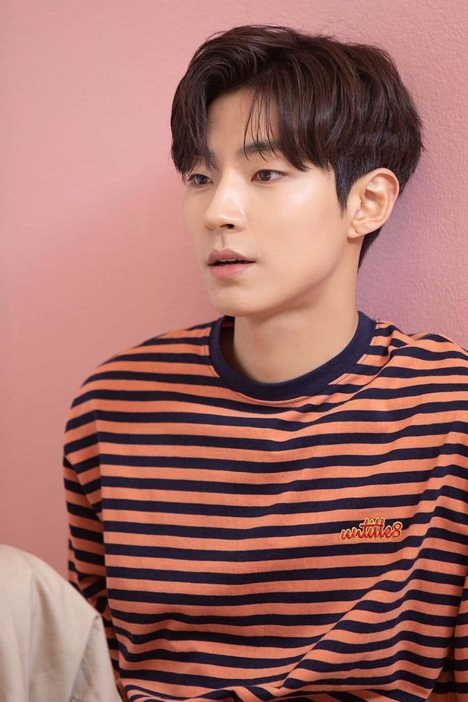 A Young Man In A Striped Shirt Leaning Against A Pink Wall Wallpaper