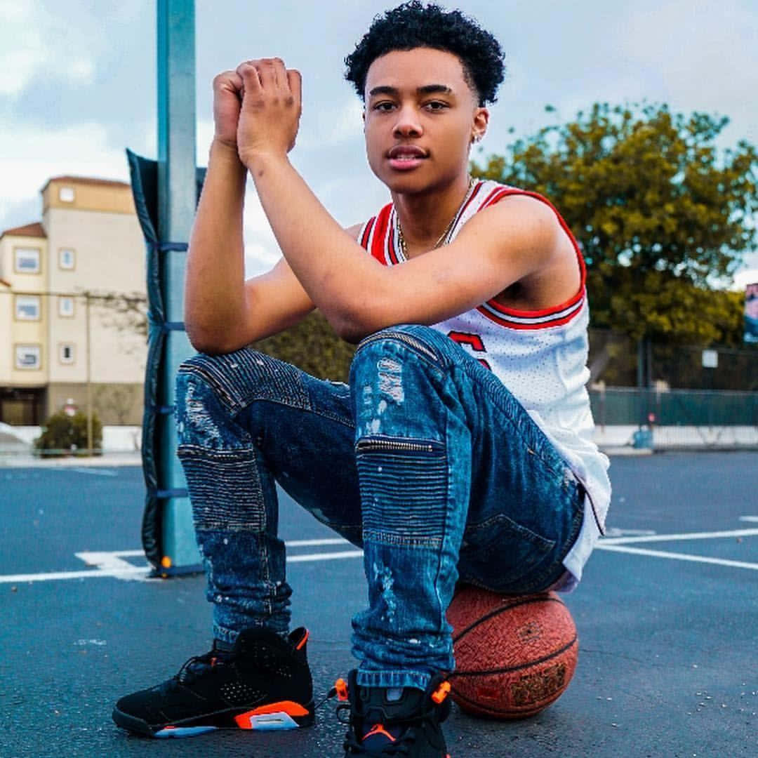 A Young Man Sitting On A Basketball Ball Wallpaper