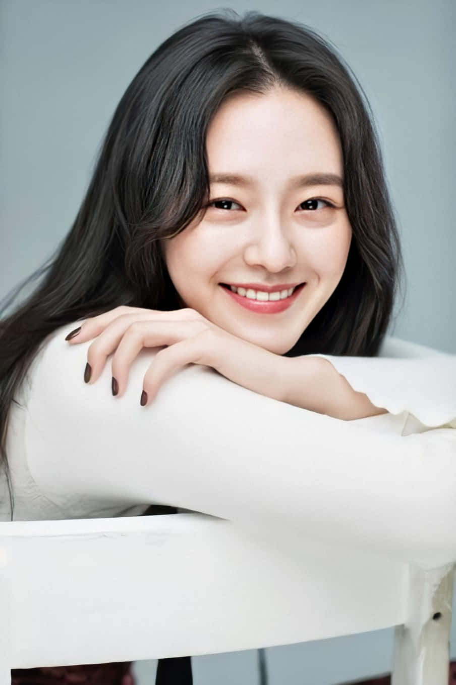 A Young Woman Smiling While Sitting On A Chair Wallpaper