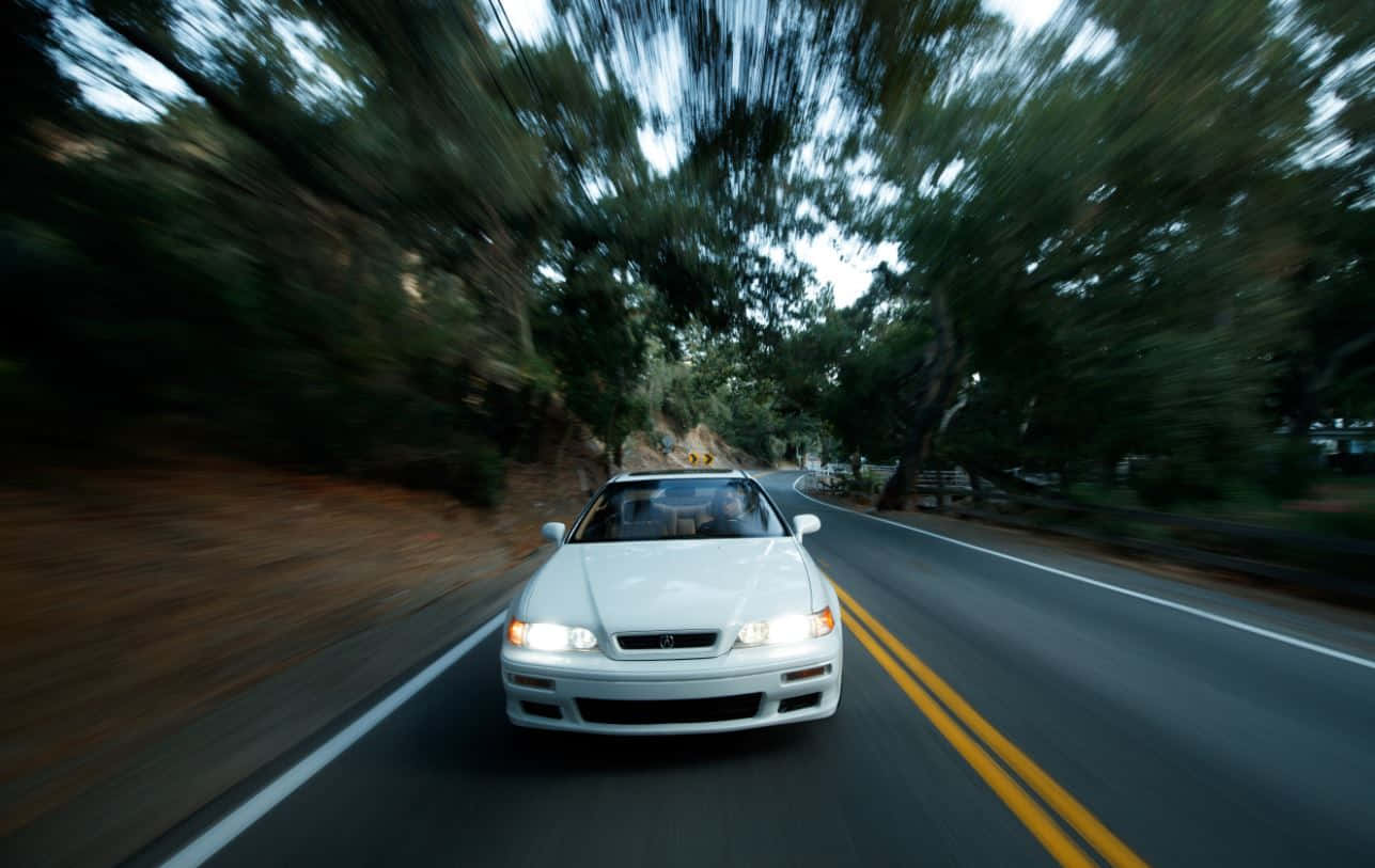 Acura Vigor Speeding Through Wooded Roadway Wallpaper