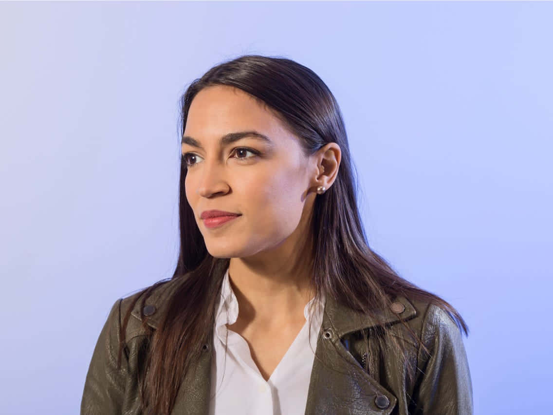 Alexandria Ocasio-cortez In Front Of Blue Backdrop Wallpaper