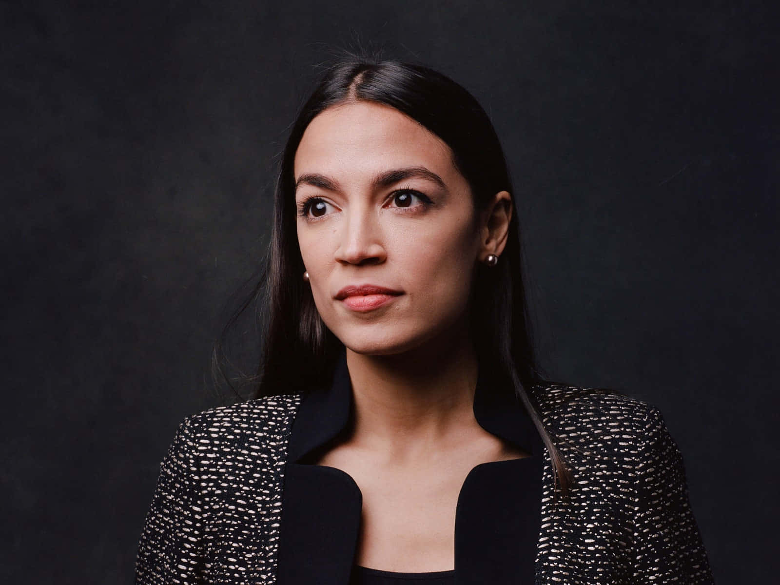 Alexandria Ocasio-cortez Posing Against A Black Backdrop Wallpaper