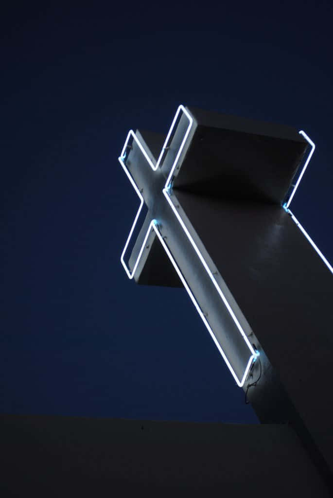 An Illuminated Neon Cross Surrounded By Darkness. Wallpaper