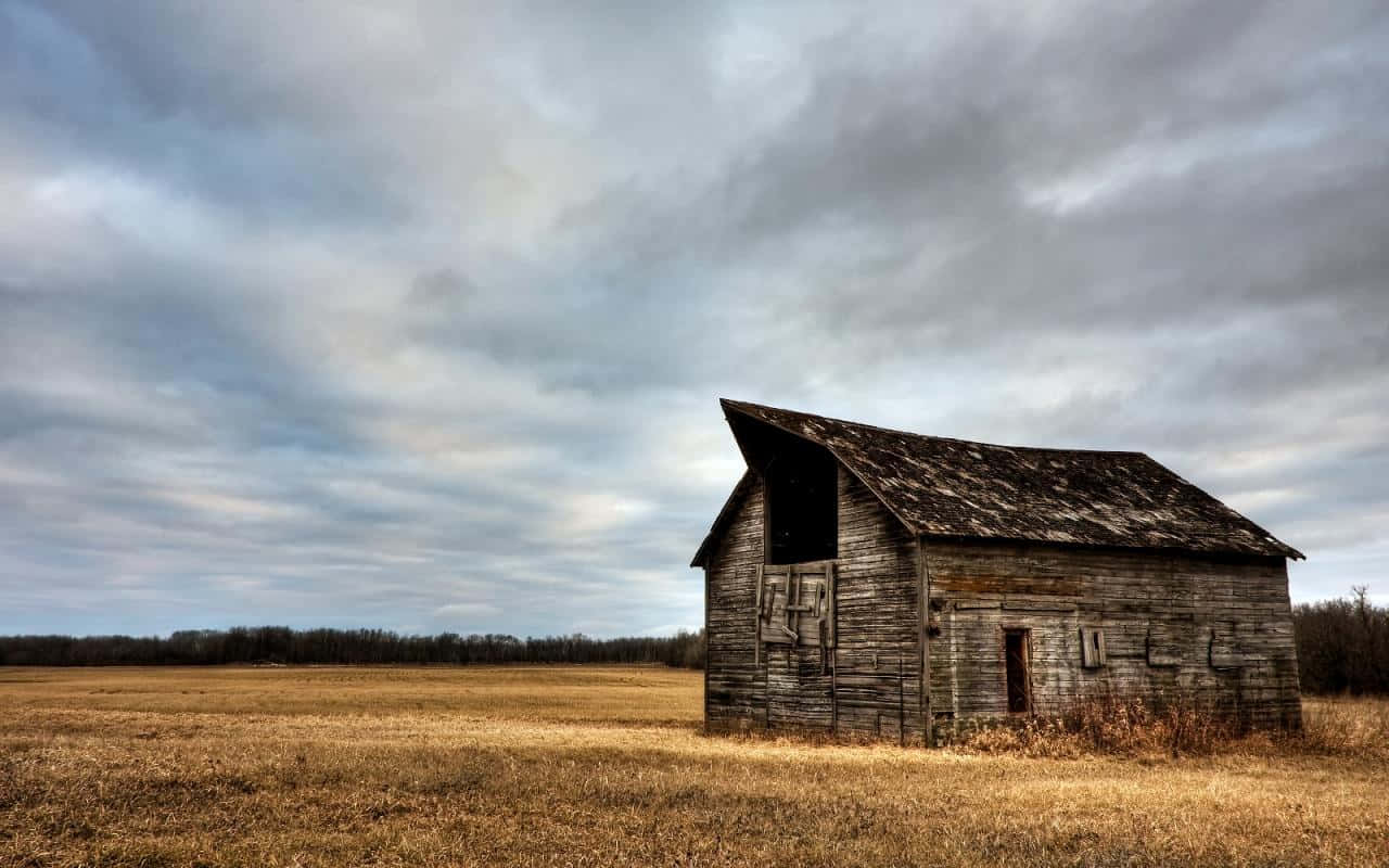 An Old Barn Sits In A Field Under A Cloudy Sky Wallpaper