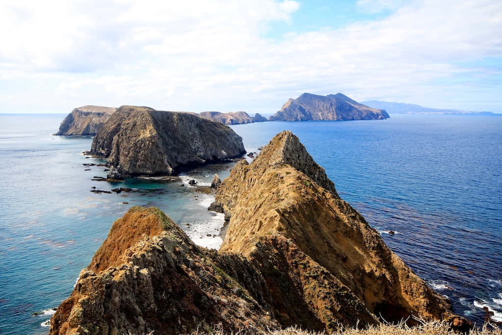 Beautiful Californian Island Landscape With Crystal Blue Waters, Green Rugged Hills, And A Stunning Sunset. Wallpaper