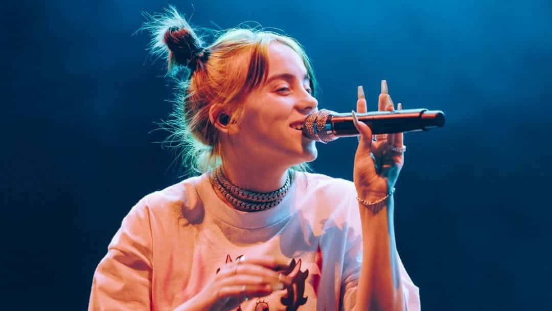 Billie Eilish Sits Surrounded By Her Laptop And Gear Wallpaper