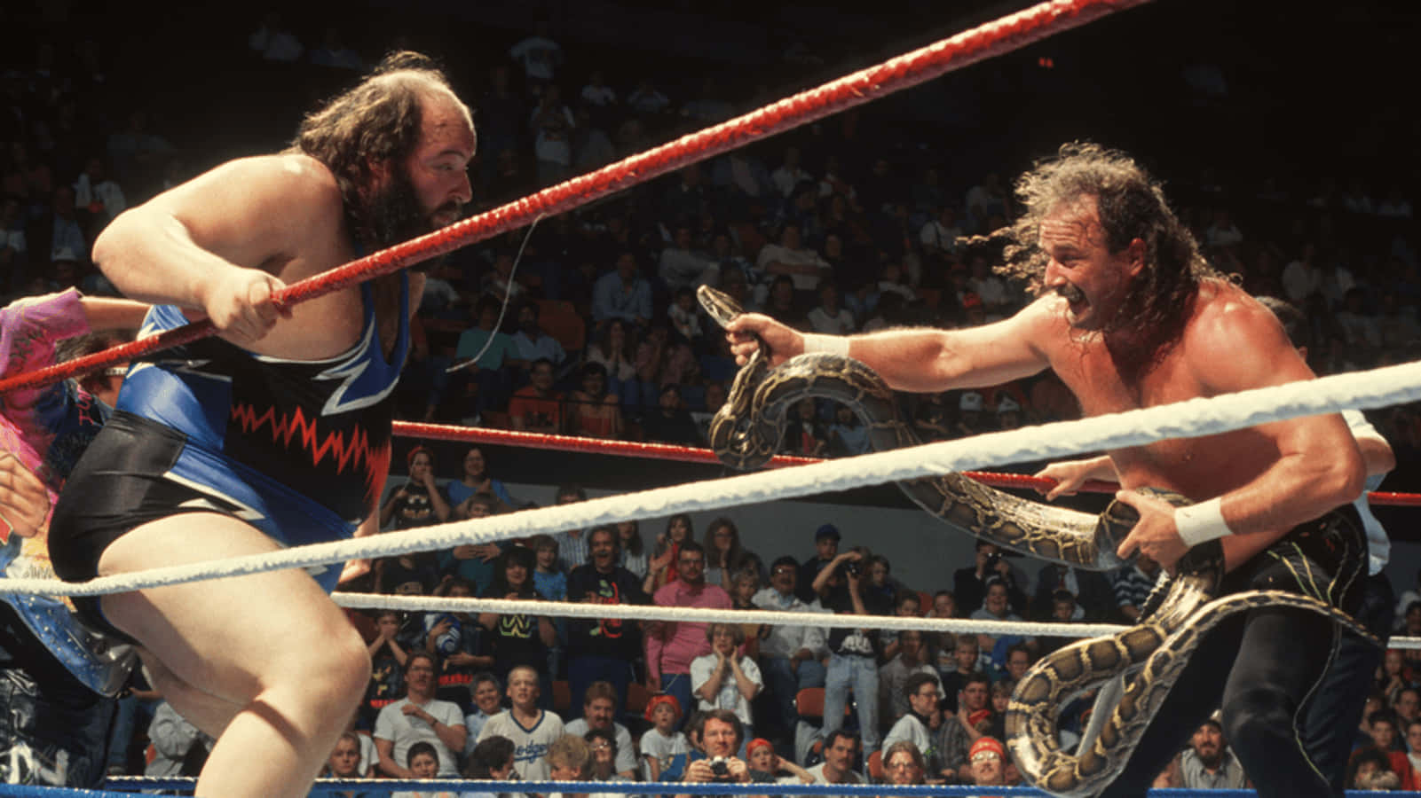 Caption: American Professional Wrestler, Jake Roberts, Threatening John Tenta In Classic Wrestling Match Wallpaper