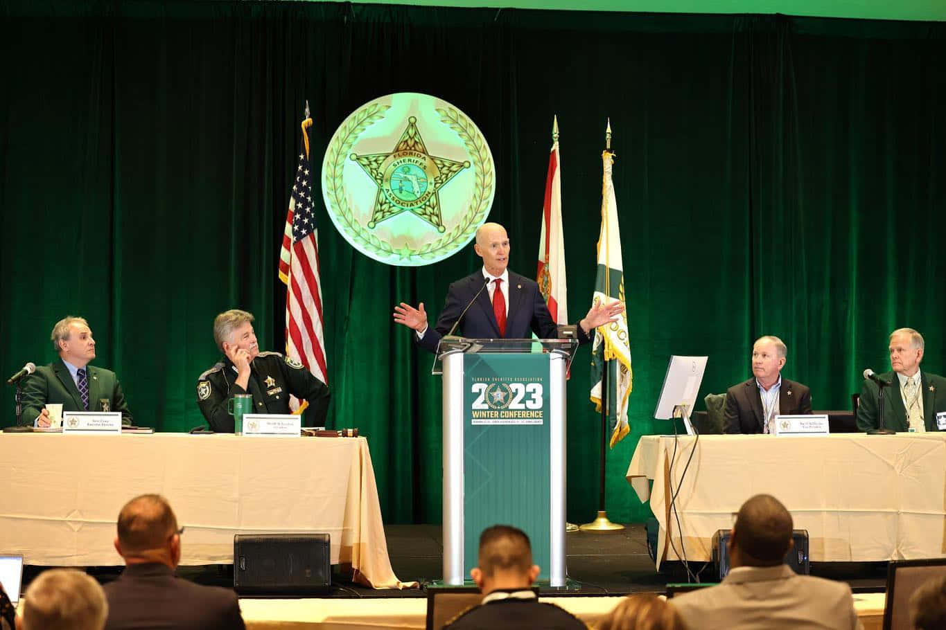 Caption: Rick Scott Delivering Speech Before Audience Wallpaper