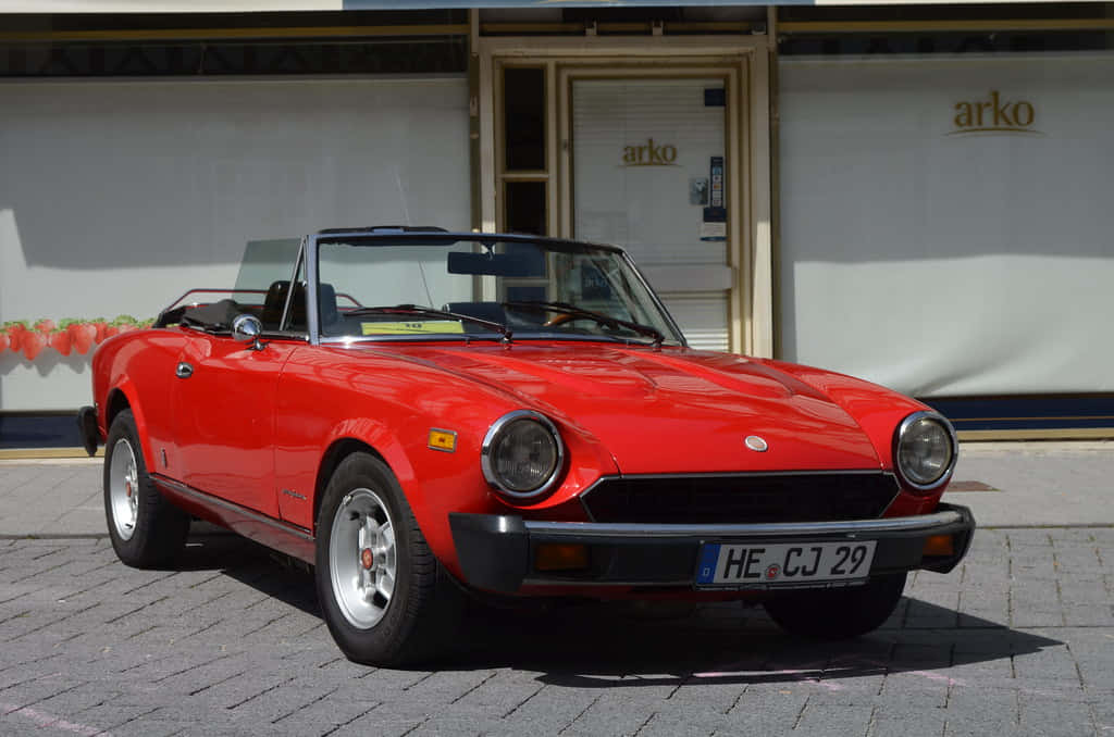 Caption: Stunning Red Fiat 124 Spider Cruising In Style Wallpaper