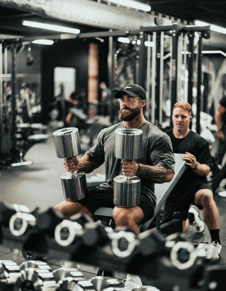 Chris Bumstead Holding Two Large Dumbbells Wallpaper