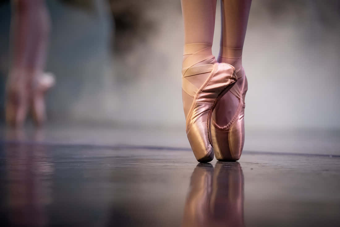 Dancer Effortlessly Gliding Across A Stage In A Pair Of Pointe Shoes. Wallpaper