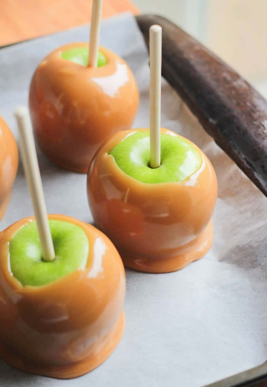 Delectable Caramel Apples On A Wooden Table Wallpaper