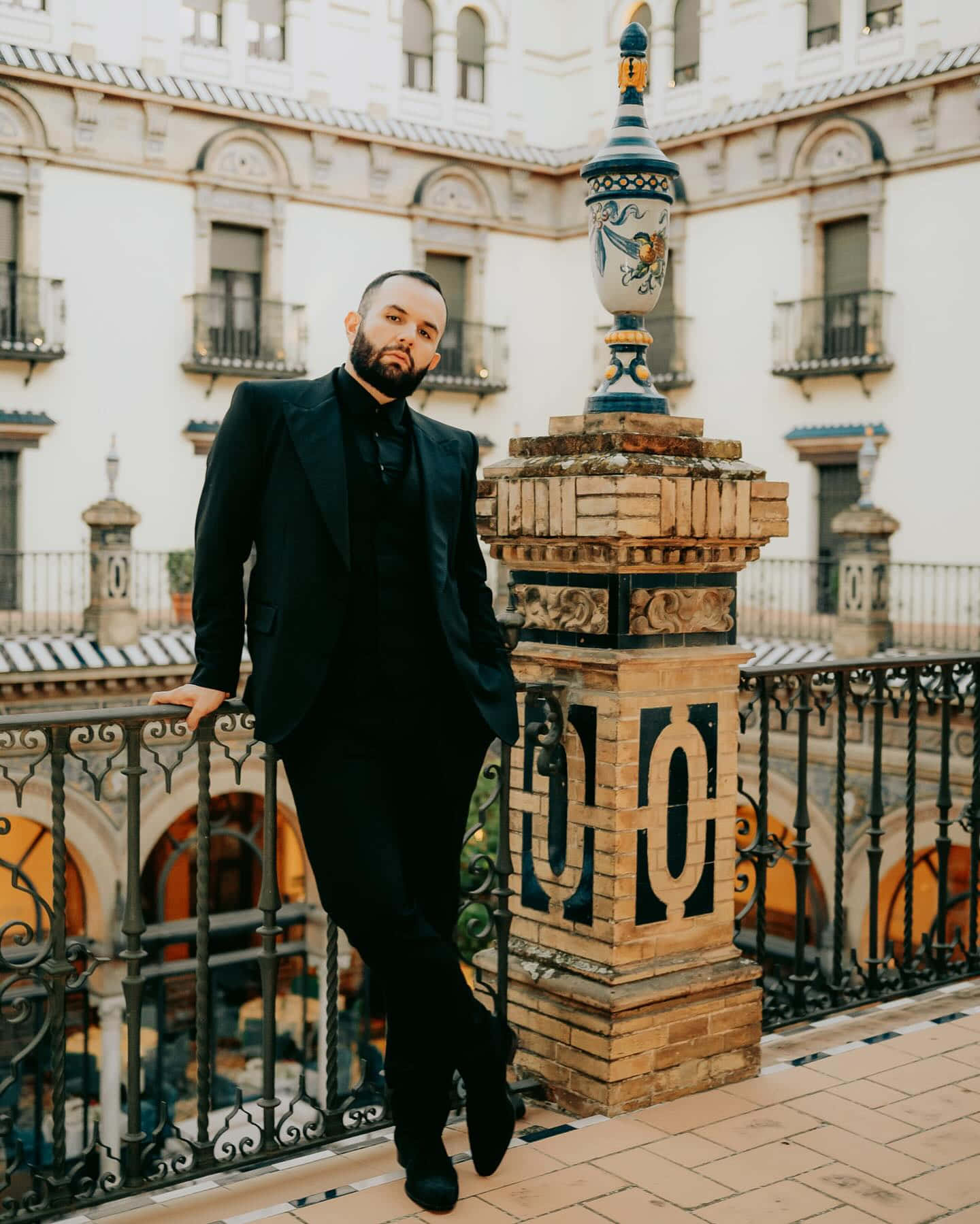 Elegant Manin Black Suit Standing Near Ornate Balcony Wallpaper