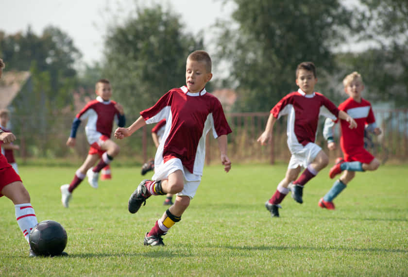 Excited Kids Playing Soccer In Green Field Wallpaper