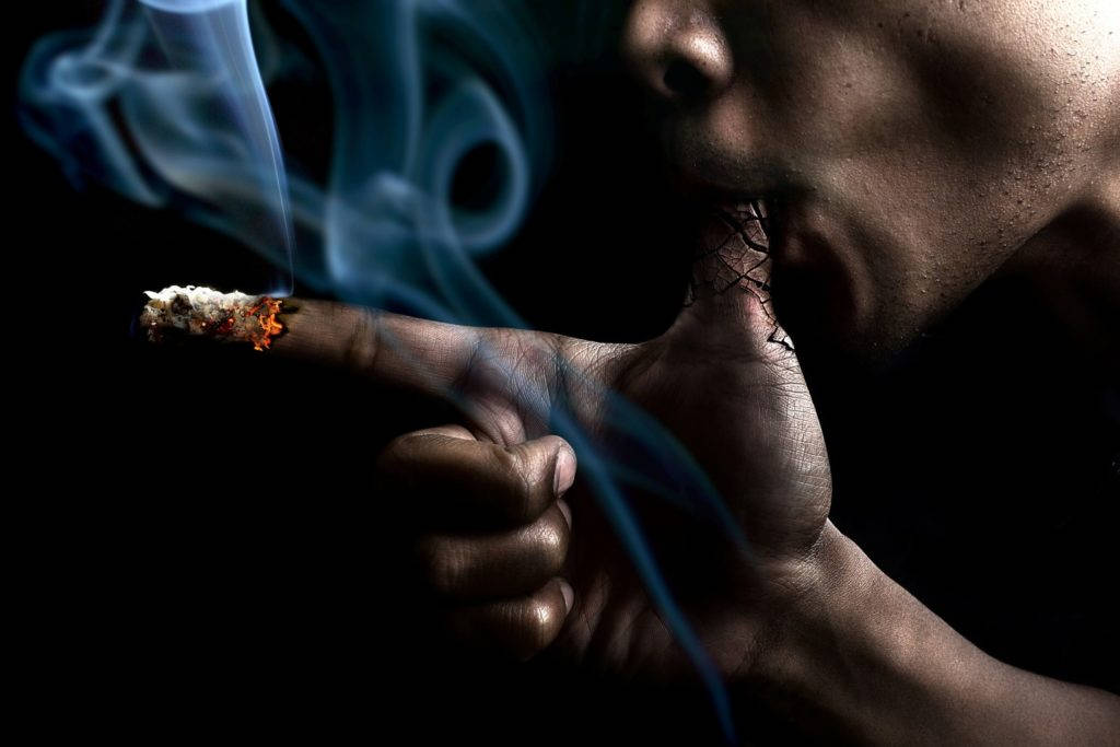 Hand Holding A Smoldering Cigarette Against A Dark Background Wallpaper