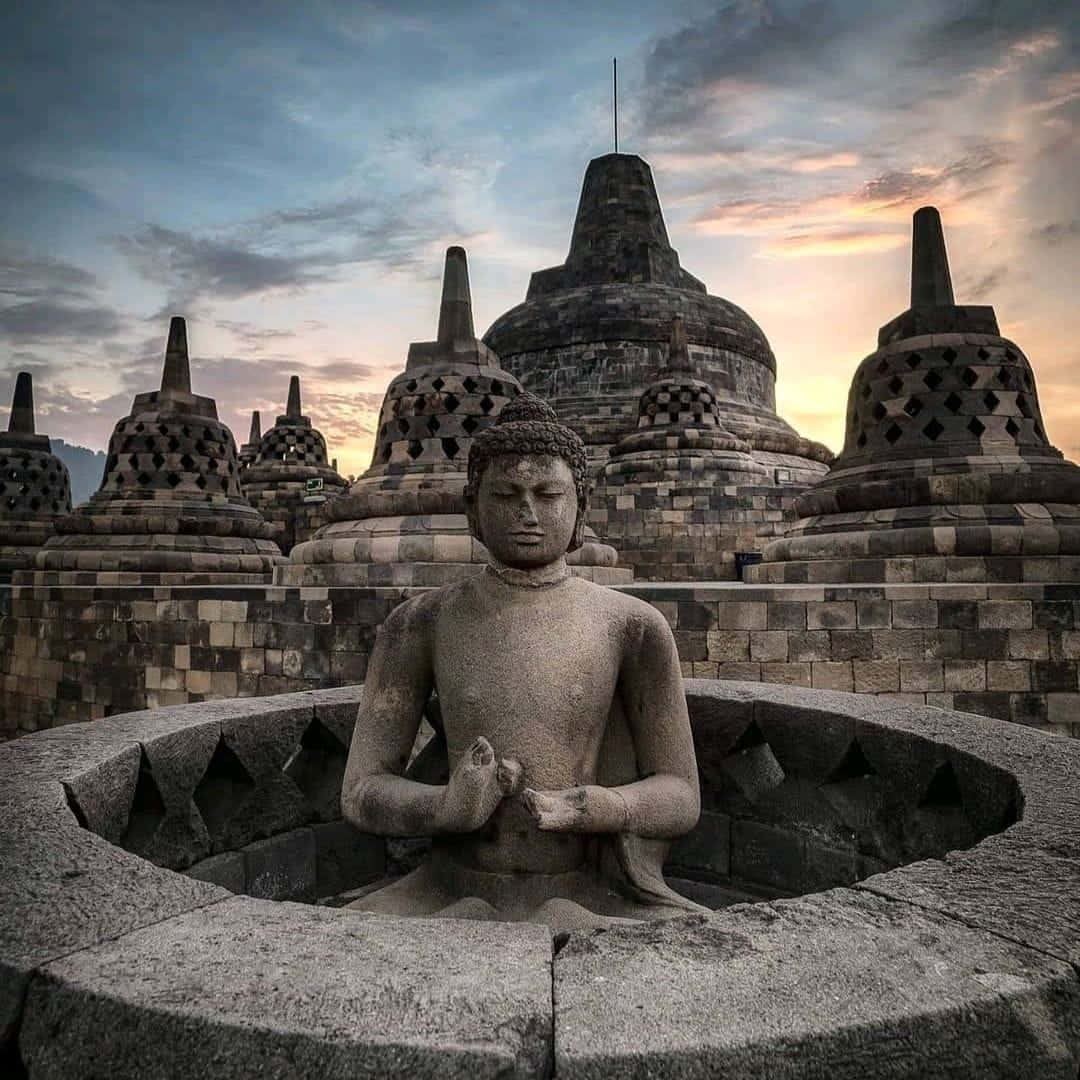 Harmonious Serenity: A Statue Of Buddha Overlooking The Magnificent Borobudur Temple Wallpaper