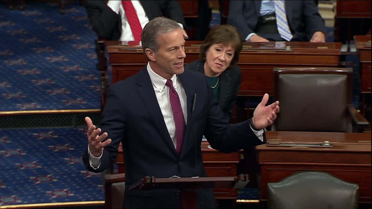 John Thune Shrugging At A Podium Wallpaper