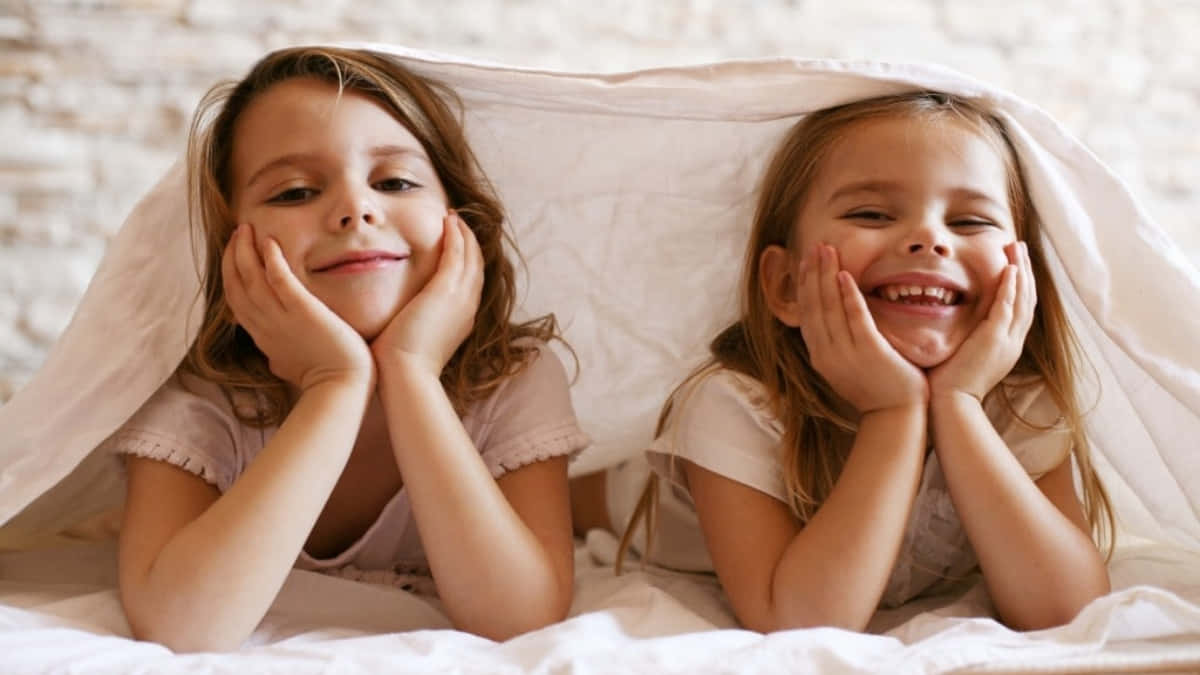 Joyful Sisters Under Blanket Wallpaper