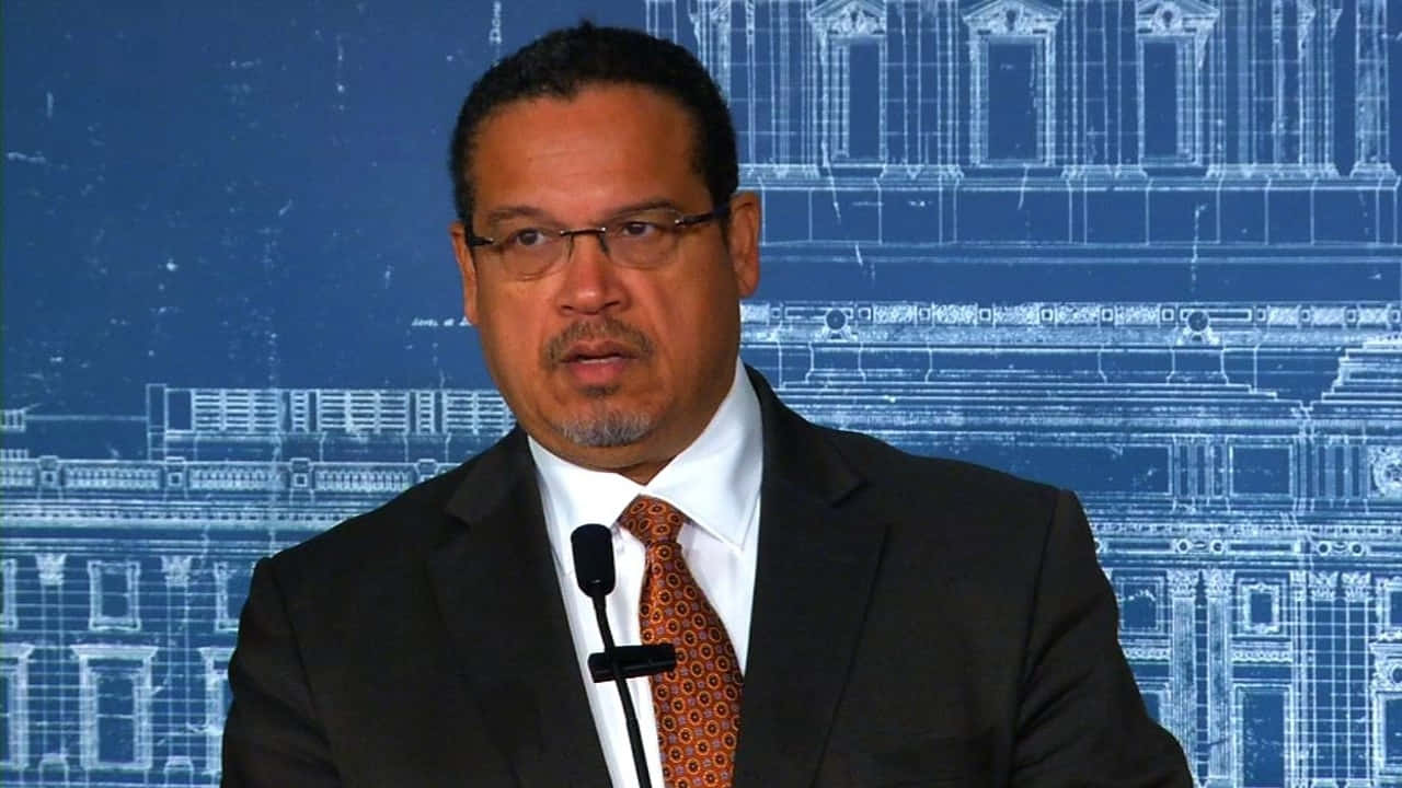 Keith Ellison Holding A Blueprint Against A Blue Background Wallpaper