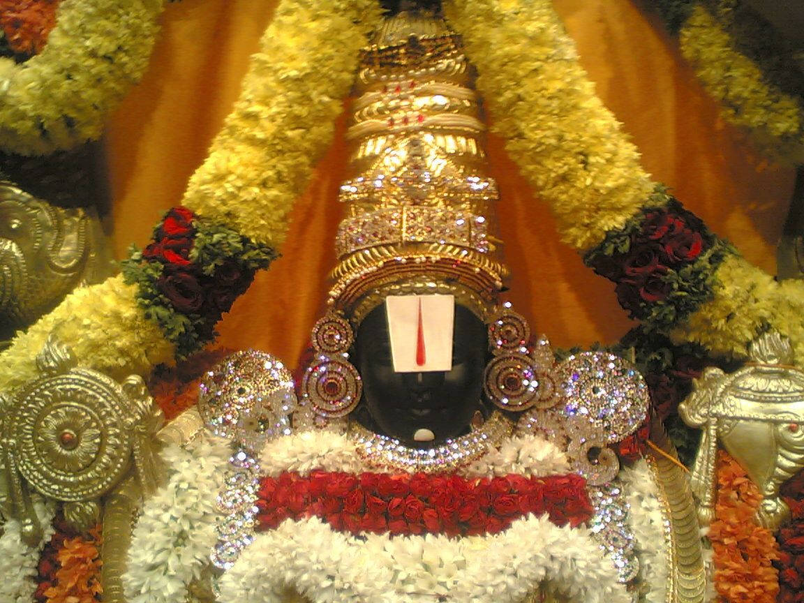 Majestic Tirupati Balaji Statue Adorned With Vibrant Flower Garlands Wallpaper