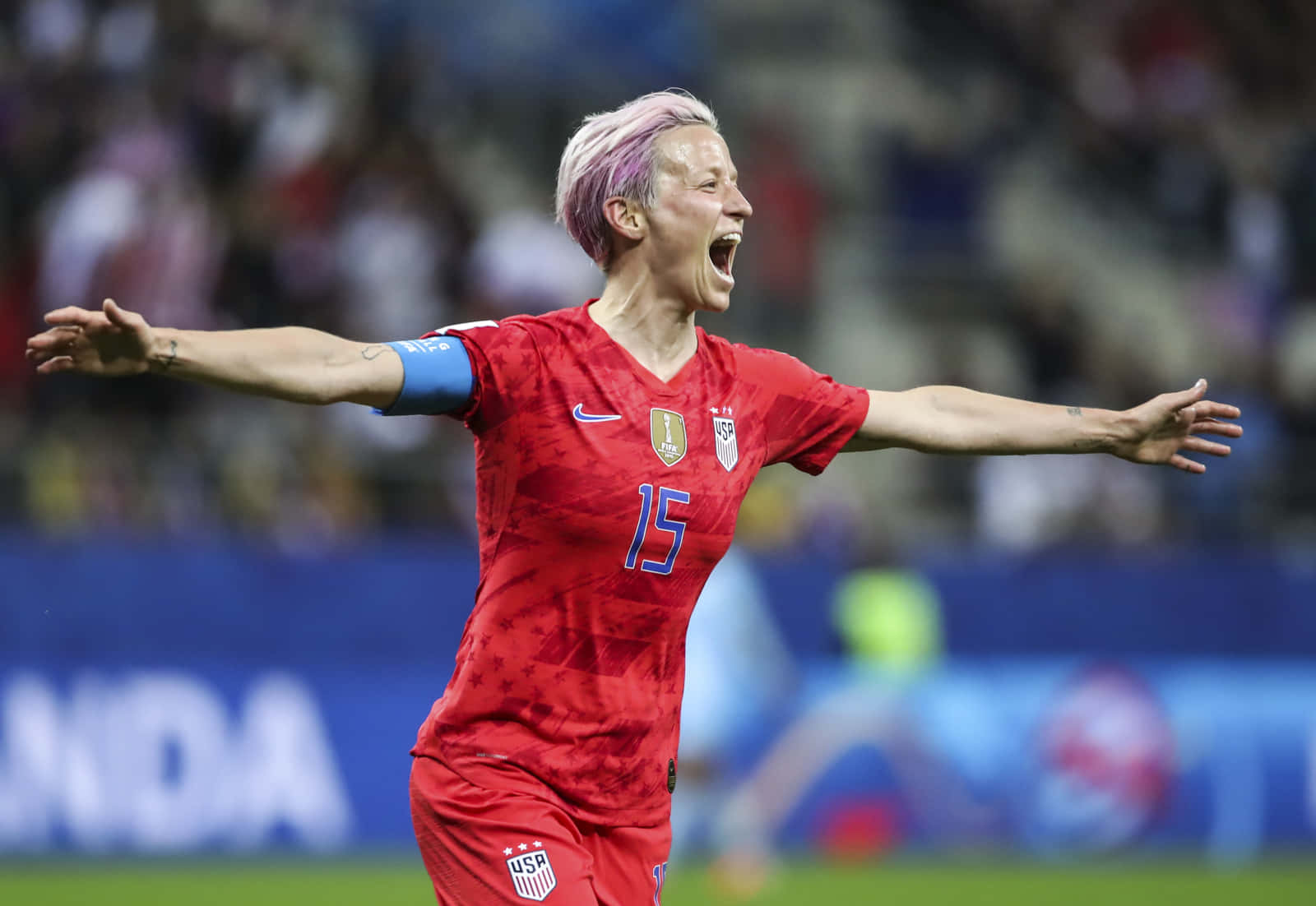 Megan Rapinoe Triumphantly Raises Her Arms On The Soccer Field. Wallpaper