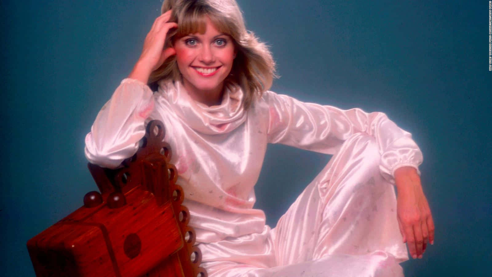 Olivia Newton John Sitting On Wooden Chair Wallpaper