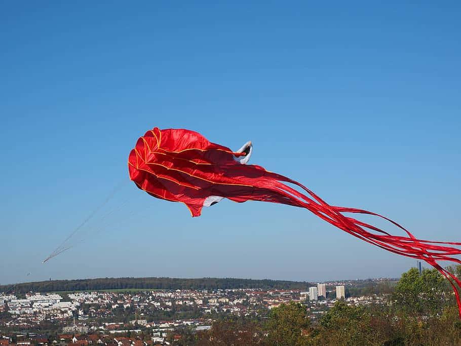 Red Squid Kite Flying Above Cityscape Wallpaper