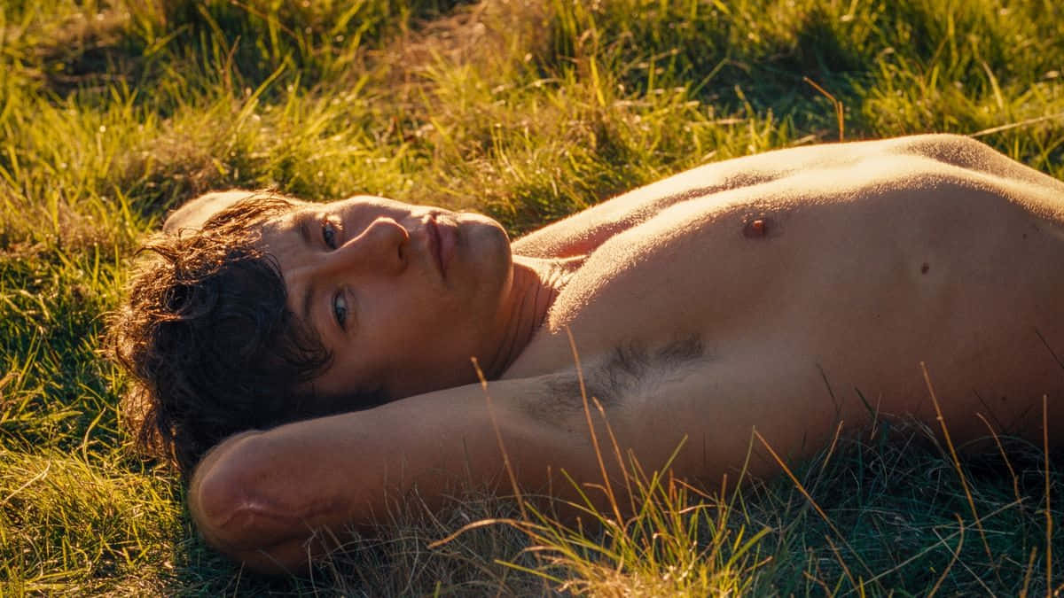 Shirtless Man Lyingin Grass During Golden Hour Wallpaper